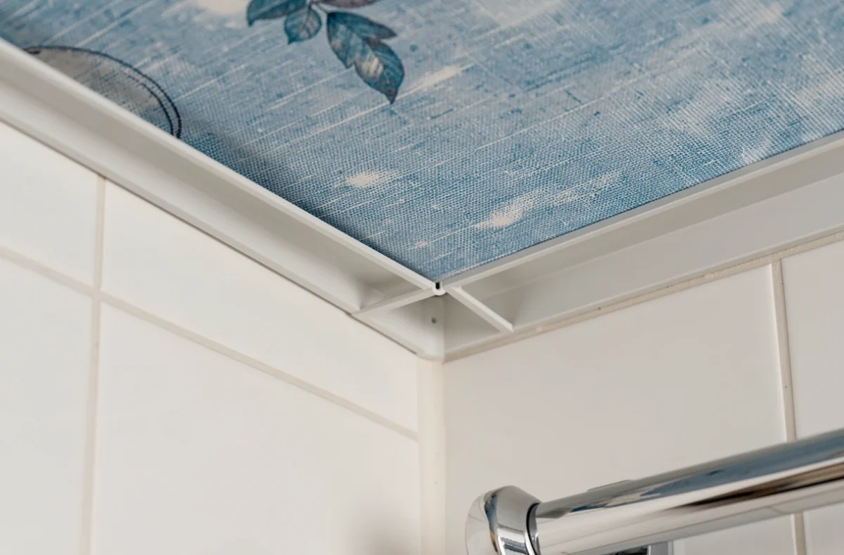 Détail d'angle d'un plafond toile tendue dans une salle de bain avec rail aluminium et surface textile étanche