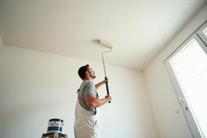 Peintre professionnel appliquant de la peinture blanche mate au rouleau sur un plafond de 50m2 dans un salon en rénovation