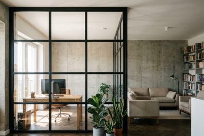 Verrière industrielle noire séparant un bureau et un salon dans un appartement contemporain avec parquet en chevrons